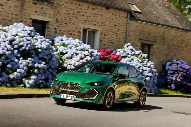 Renault Clio 6 verte de profil devant une maison en pierre fleurie d'hortensias