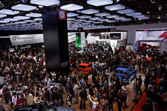 Foule de visiteurs entre les stands et les voitures d'un hall du Mondial de l'Auto à Paris