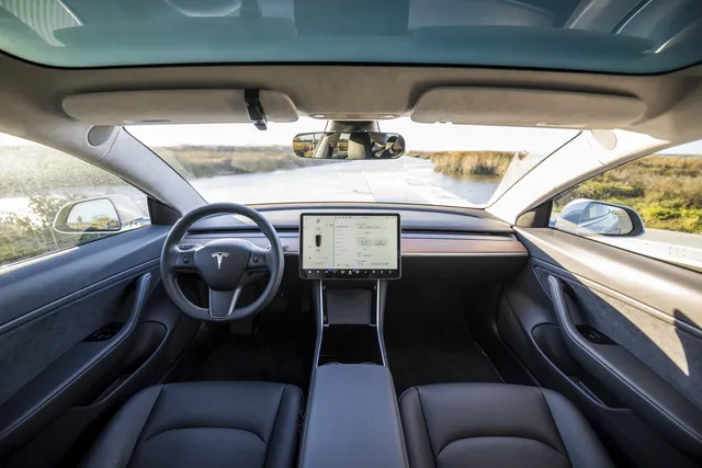 Intérieur d'une Tesla Model 3 : volant, grand écran central et route visible à travers le pare-brise