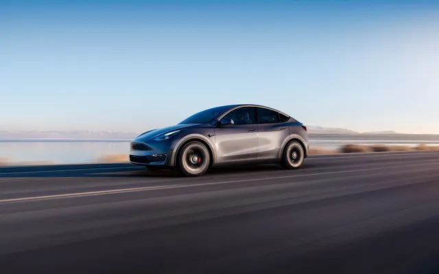 Tesla Model Y electrique grise roulant sur une route au coucher du soleil