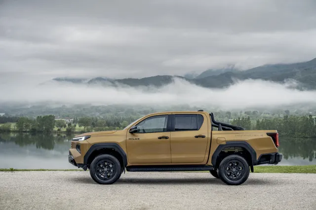 Le nouveau Toyota Hilux 2026 de profil au bord d'un lac, finition Invincible jaune