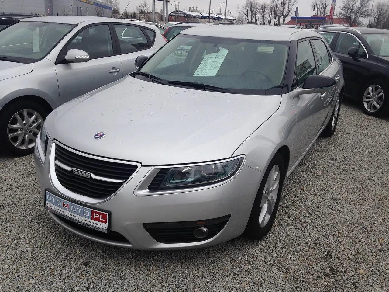 Saab 9-5 grise de trois quarts avant sur un parc de vehicules d'occasion