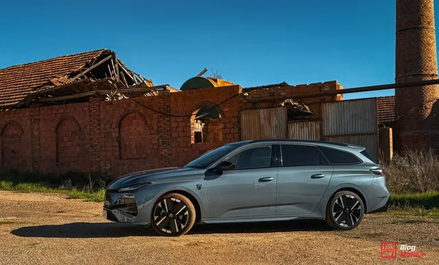 Peugeot 308 SW restylee 2026 de profil, gris ardoise, garee devant une batisse en briques